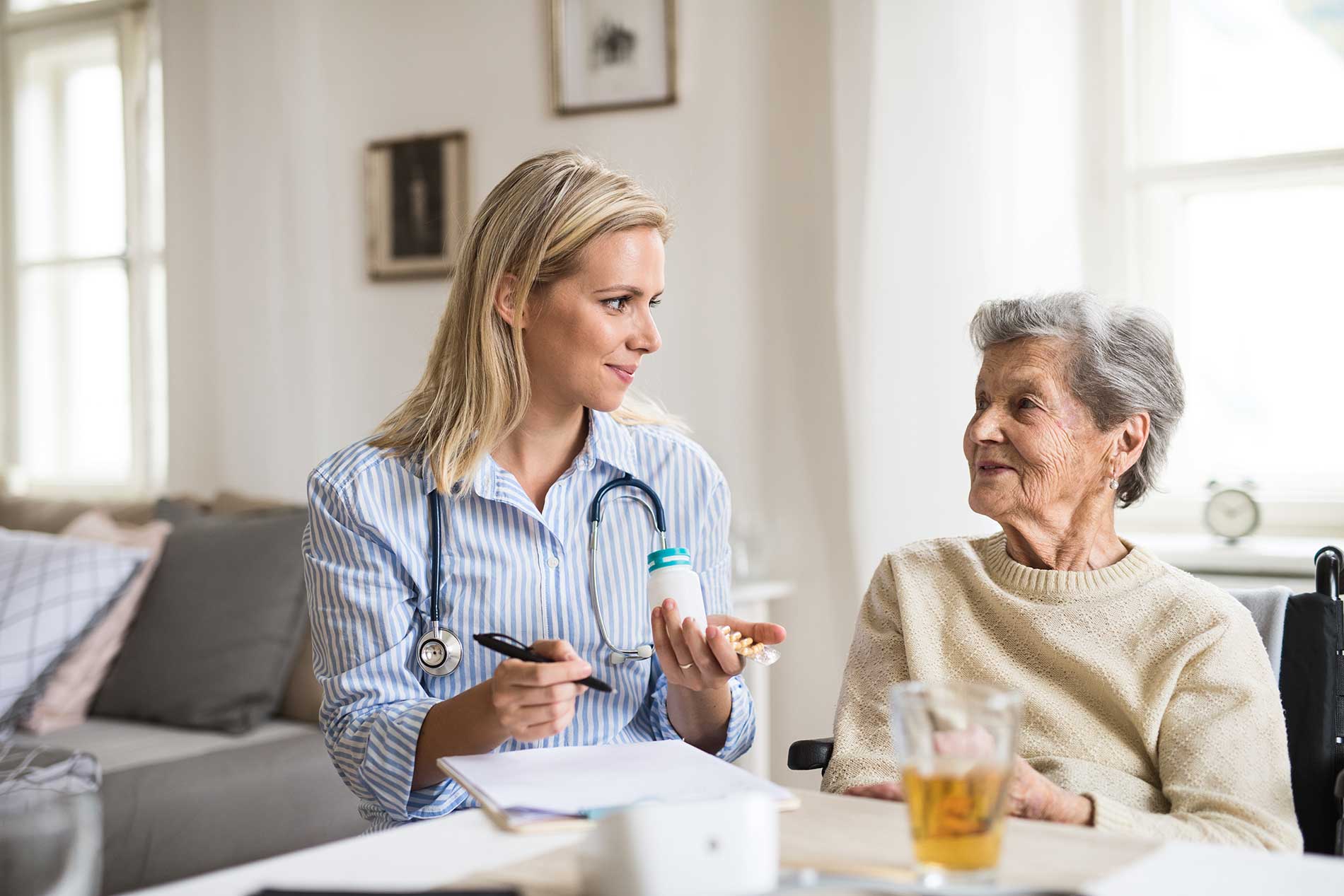 A health visitor explaining a senior woman in wheelchair how to take pills