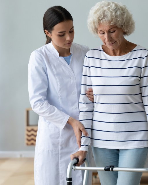 Young woman caregiver helping disabled old grandma patient using walker